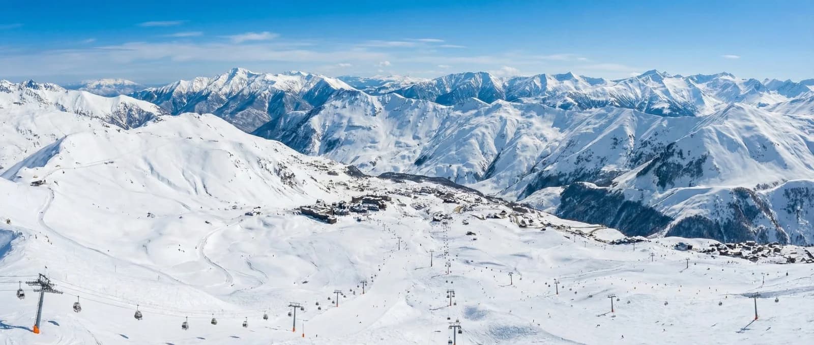 מבט פנורמי ממעוף ציפור על אתר סקי מושלג, פסגות הרים לבנות ומעליות סקי תחת שמיים כחולים